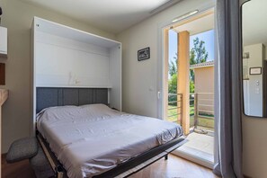 Ein Schlafzimmer mit Bett, eingebautem Kleiderschrank, einer Glastür zum Balkon und einem kleinen Nachttisch.