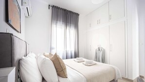 Een moderne slaapkamer met een bed, witte gordijnen, een kledingkast en een wandairconditioner.