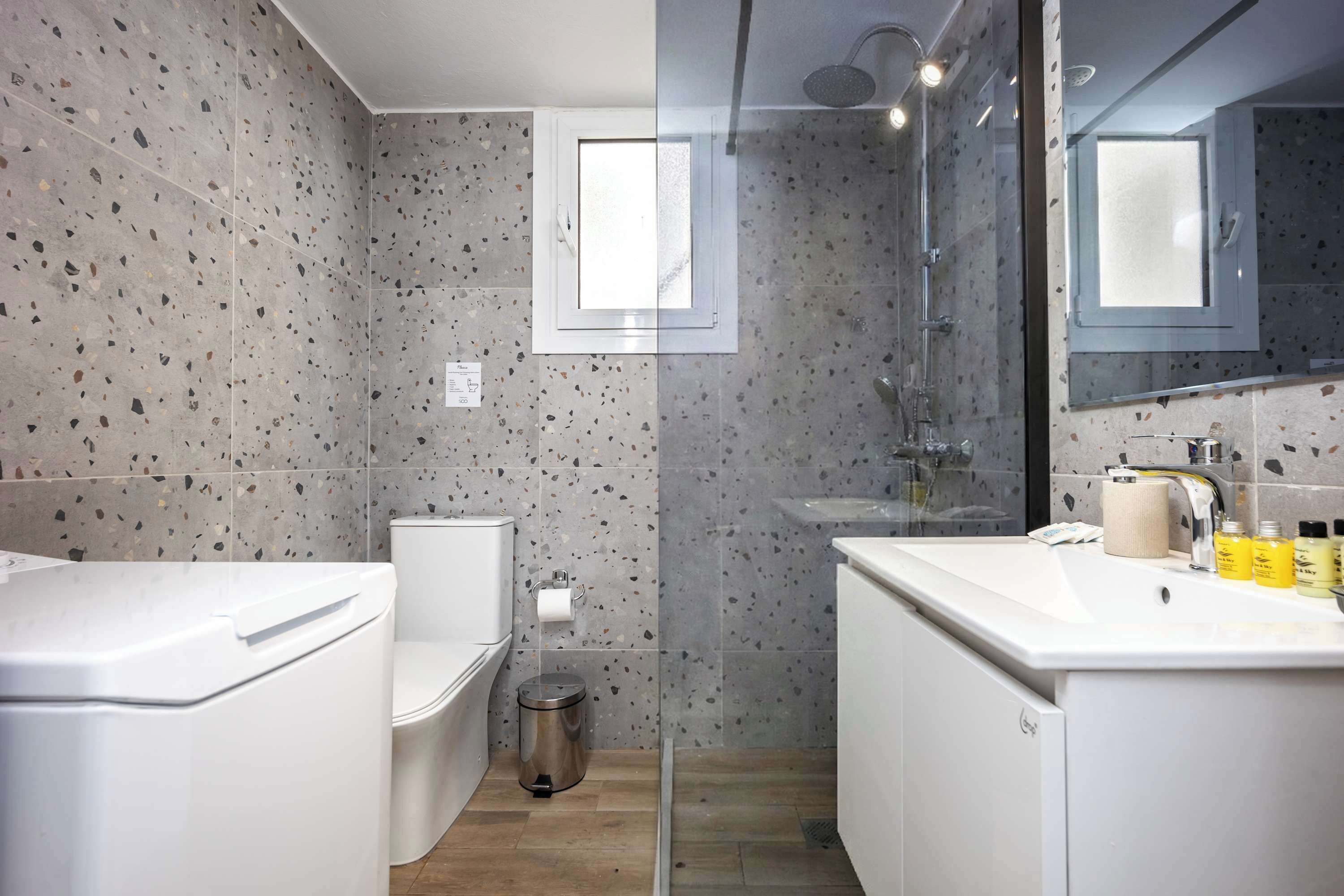 Un baño moderno con inodoro, bidé y lavamanos, con baldosas veteadas y cabina de ducha de vidrio.