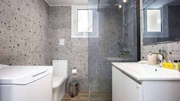 Un baño moderno con inodoro, bidé y lavamanos, con baldosas veteadas y cabina de ducha de vidrio.