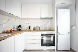 Une cuisine moderne avec des meubles blancs, un plan de travail en bois, un four encastré et un réfrigérateur blanc.
