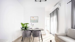 Een moderne woonkamer met een grijze bank, een eethoek met een tafel en stoelen, en een groot raam met gordijnen.