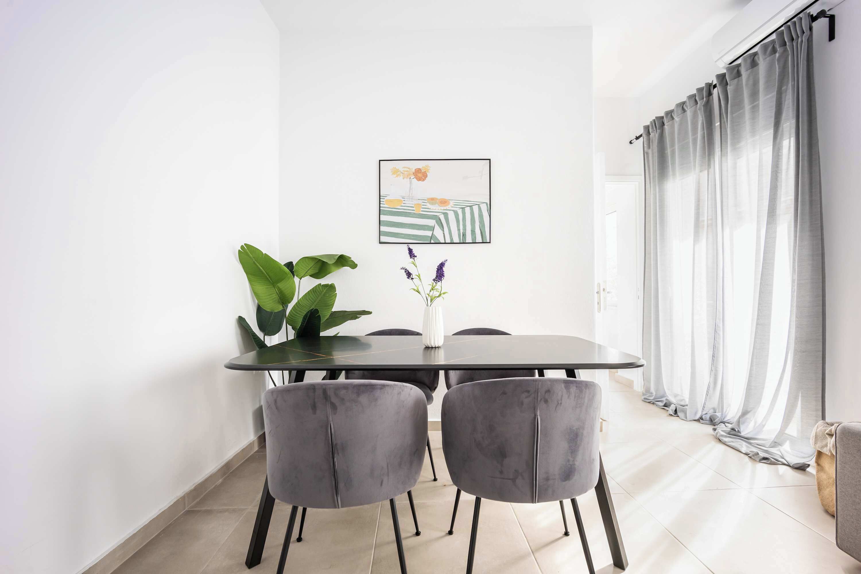Un comedor con una mesa, sillas, una planta y un cuadro en la pared.