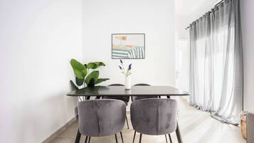 Un comedor con una mesa, sillas, una planta y un cuadro en la pared.