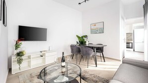 Een moderne woonkamer met een flatscreen televisie, een eethoek met een tafel en stoelen, en een bank.