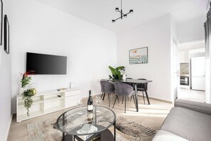 Uma sala de estar moderna com uma TV de tela plana, uma área de jantar com mesa e cadeiras, e um sofá.