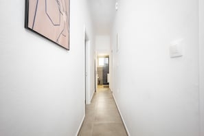 Un couloir étroit aux murs blancs, orné d’un tableau abstrait encadré et muni d’un interrupteur.