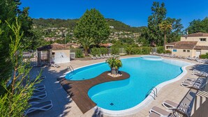 Uma piscina com deck de madeira, cadeiras de descanso e vista para uma cidade no topo da colina.