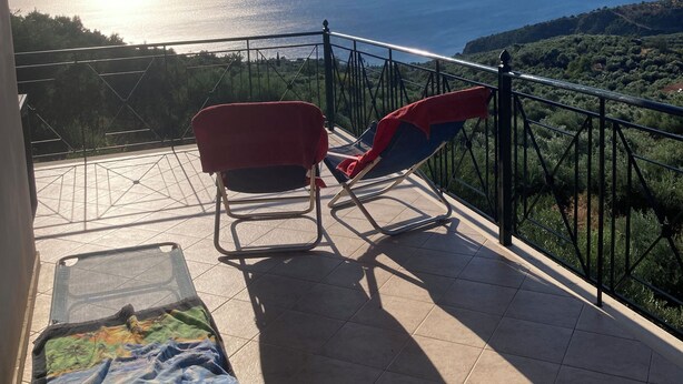 A balcony with two chairs and a small table, overlooking a scenic view of a body of water and distant mountains.