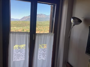 A room with a view of a mountainous landscape through a window with curtains. - Endless blue (Kitries)
