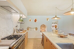 A kitchen with a gas stove, wooden cabinets, marble countertops, pendant lighting, and decorative wall art. - Les 3 thyms - Avec Piscine Privée - (Méounes-lès-Montrieux)