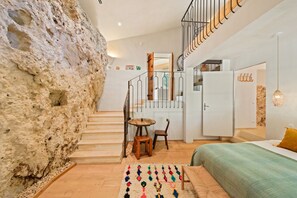 A modern interior with a stone wall, a staircase, a bed, and a dining area. - Les 3 thyms - Avec Piscine Privée (Méounes-lès-Montrieux)