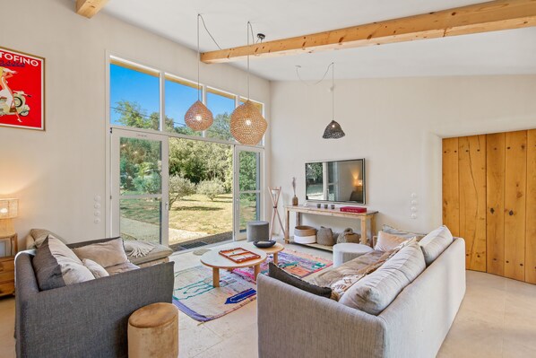 A modern living room with a large glass door leading to a garden, a sofa set, a coffee table, and hanging pendant lights. - Les 3 thyms - Avec Piscine Privée - (Méounes-lès-Montrieux)