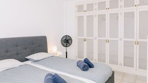 A bedroom with a grey upholstered headboard, a bed with grey linens, two rolled towels, a bedside table with a lamp, and a white wardrobe with perforated panels. - Bright 1-Bedroom Apartment with Private Terrace and Views | Pool (Playa de las Américas)