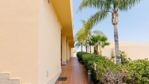 A corridor with a tiled floor, beige walls, and a row of palm trees. - Bright 1-Bedroom Apartment with Private Terrace and Views | Pool (Playa de las Américas)