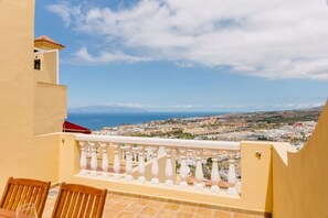 A balcony with a view of a coastal town, a table with chairs, and a red roof. - Bright 1-Bedroom Apartment with Private Terrace and Views | Pool (Playa de las Américas)