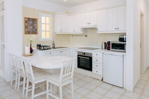A kitchen with white cabinets, a built-in oven, a microwave, and a dining area with white chairs. - Bright 1-Bedroom Apartment with Private Terrace and Views | Pool (Playa de las Américas)