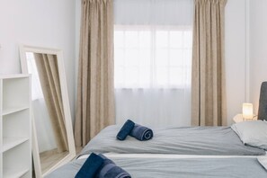 A hotel room with two beds, a bedside table with a lamp, a wardrobe, and a window with curtains. - Bright 1-Bedroom Apartment with Private Terrace and Views | Pool (Playa de las Américas)