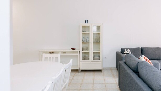 A minimalist living space with a white dining table, a gray sofa, and a cabinet with glass doors. - Bright 1-Bedroom Apartment with Private Terrace and Views | Pool (Playa de las Américas)