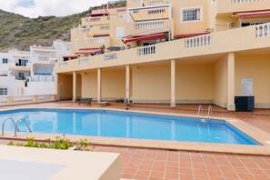 A swimming pool with a tiled deck, a bench, and a lifeguard stand. - Bright 1-Bedroom Apartment with Private Terrace and Views | Pool (Playa de las Américas)