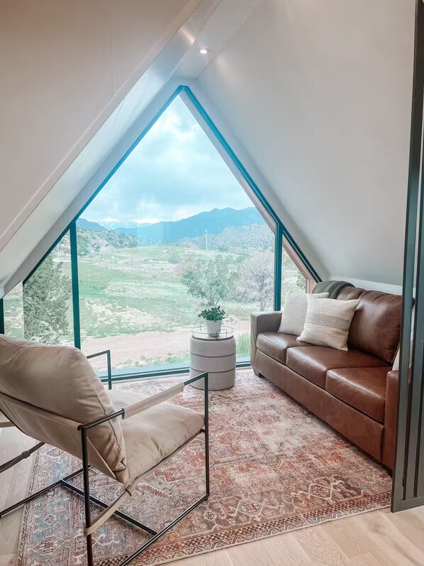 A modern loft bedroom with a large skylight, a brown leather sofa, a beige armchair, and a patterned rug. - #2 Peakview @ Royal Gorge (Cañon City)