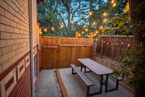 A patio with a wooden fence, a bench, and string lights.