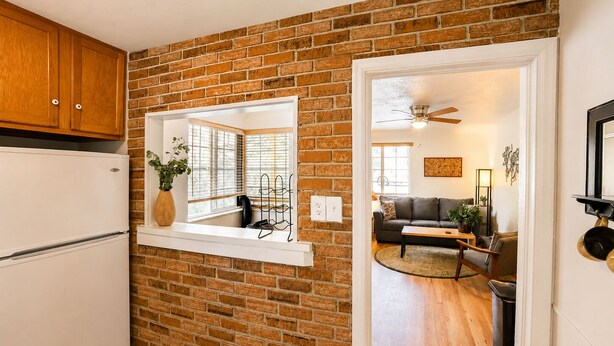 A kitchen with a brick wall, wooden cabinets, a window with blinds, and a ceiling fan. - Stay In The Quiet Side of Denver by Sloan’s Lake (Denver)