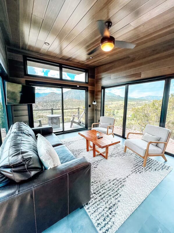 Ein großzügiges Wohnzimmer mit einer Ledersofa, zwei Sesseln, einem Holztisch und großen Fenstern mit Blick auf die Landschaft.