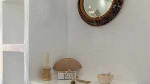 A white console table with a round mirror, a candle holder, a small box, a fan, and a mortar and pestle.