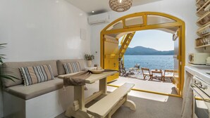 A room with a sofa, a table, a bench, and a view of the sea through an open archway.