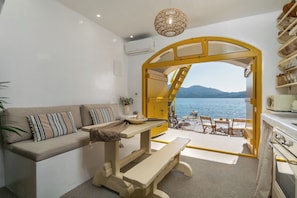 Une piÚce comprenant un canapé, une table, un banc et offrant une vue sur la mer par une arche ouverte.