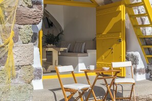 A yellow door leading to a room with a sofa, two chairs, a table, and a ladder. - Ky-ma Boat House (Milos)