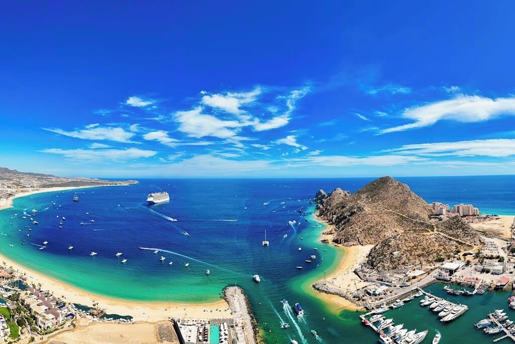An aerial view of a coastal area with a marina, a beach, and a rocky hill.