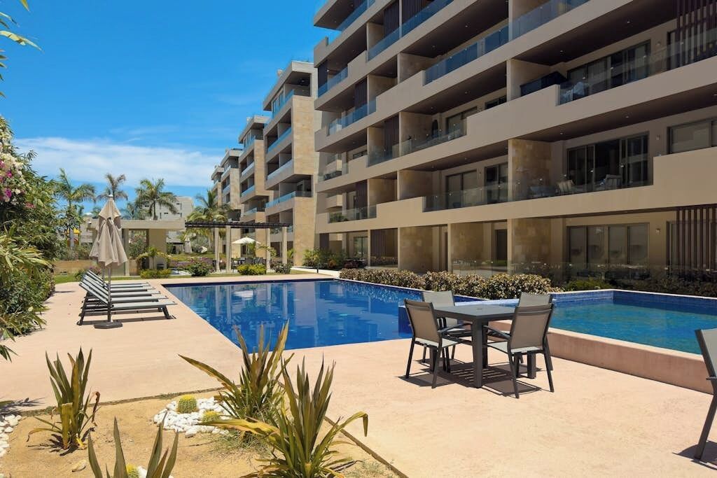 A modern hotel with a swimming pool, outdoor seating, and a view of palm trees.