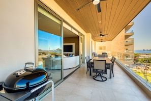 A balcony with a grill, a dining area, and a view of the city. - Bright Coastal Condo With Ocean-view Balcony, Gym, Pools, BBQ & Kids Park (Cabo San Lucas)