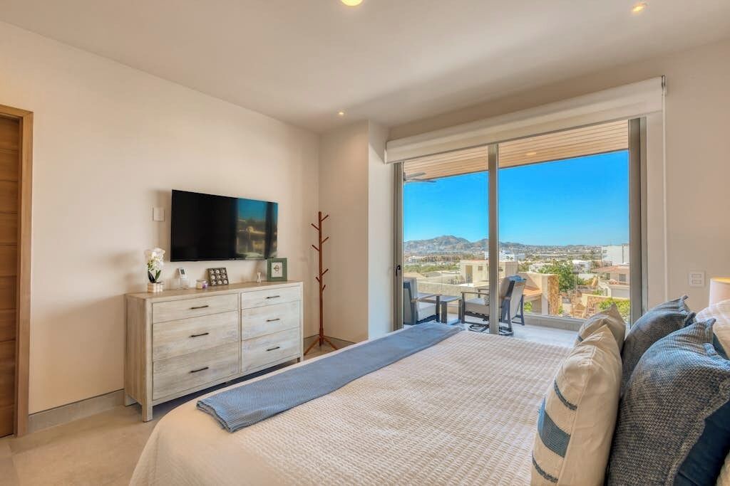 A bedroom with a bed, a TV, a dresser, and a balcony with a view.