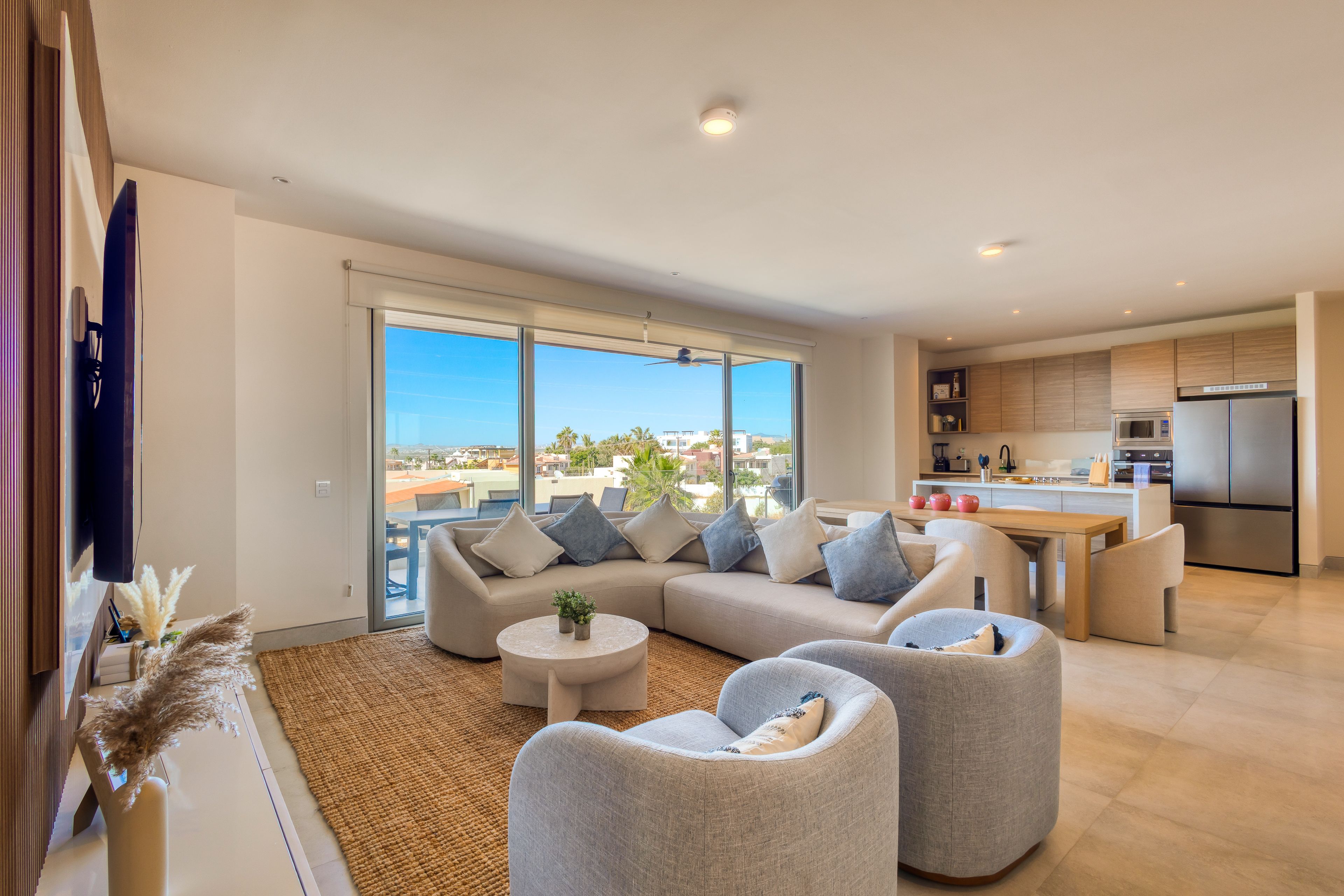 A modern living room with a sectional sofa, two armchairs, a coffee table, and a view of the city through large windows.