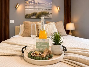 A bed with a framed picture, a bottle of orange juice, two glasses, a decorative tray with green fruits, and a small potted plant. - Cozy Escape Free Parking Private Patio (Miramar)