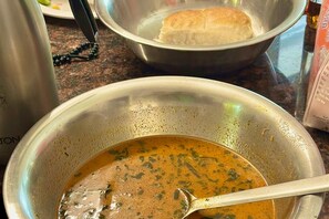 Un bol de soupe avec une cuillère, un bol en métal et une miche de pain sur un plan de travail de cuisine.