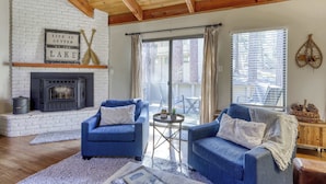 Een woonkamer met een open haard, twee blauwe fauteuils, een salontafel en uitzicht op het omliggende landschap.