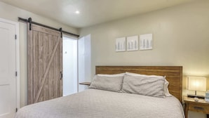 Een slaapkamer met een bed, een houten hoofdbord, een nachtkastje, een lamp en een schuifdeur.