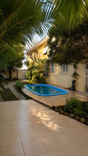 A swimming pool surrounded by a garden with palm trees and a tiled patio.