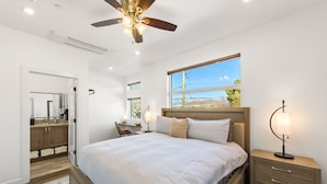 Een slaapkamer met een groot bed, een bureau, een stoel, een nachtkastje met een lamp en een raam met uitzicht op de omgeving.