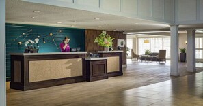 A reception desk with a modern design, a large window, and a seating area with chairs and a table. - Lake Champlain King Room with Pool & Gym (South Burlington)