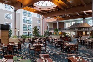 A hotel lobby with multiple dining areas, a large open space with a patterned carpet, and a view of the building's exterior. - Lake Champlain King Room with Pool & Gym (South Burlington)