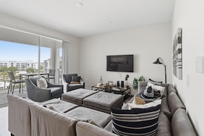 Ein modernes Wohnzimmer mit Balkon, grauem Sofa, Flachbildfernseher und minimalistischer Einrichtung.