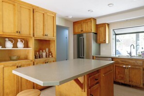 A kitchen with wooden cabinets, a stainless steel refrigerator, and a large window. - The Still House ~ Acreage · Hot Tub · Sauna · Gym (Bend)