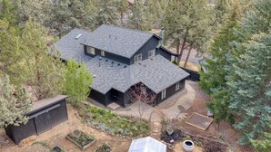 A two-story house with a dark roof, surrounded by trees and a garden. - The Still House ~ Acreage · Hot Tub · Sauna · Gym (Bend)