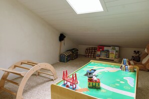 Lasten leikkialue, jossa on puinen keinuhevonen, leikkijunaset ja lastenkirjoja sisältävä kirjahylly.
