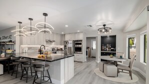 Een moderne keuken met een centraal eiland, barkrukken en een eethoek met tafel en stoelen.